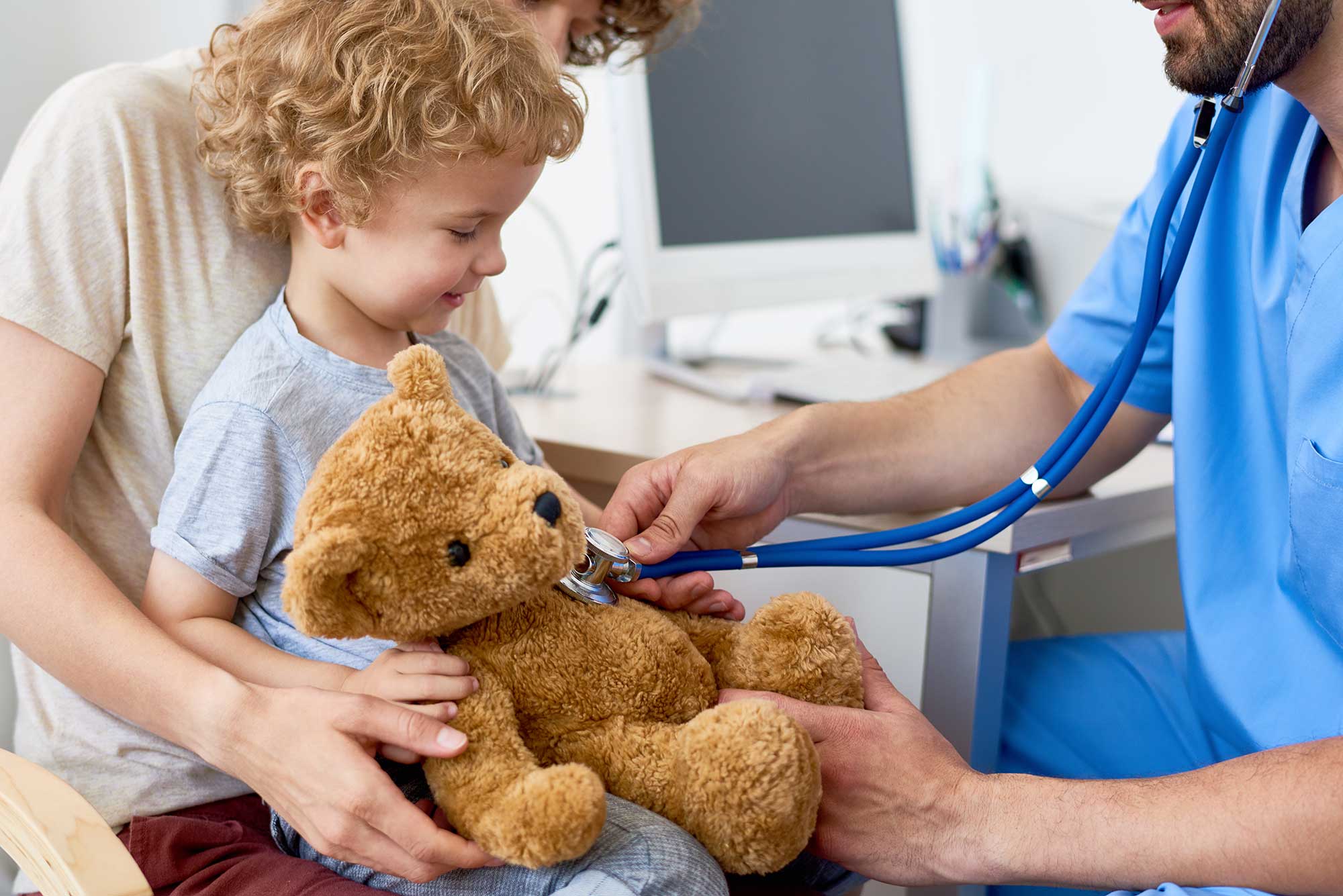 A child holds a teddy bear as a doctor examines the bear